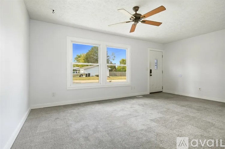 A room with a ceiling fan and a window showing a view of a house and trees.
