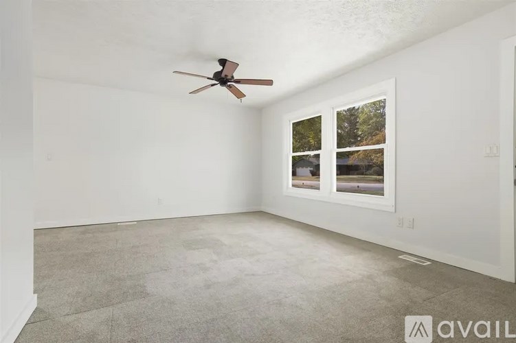 A room with a ceiling fan and a window showing a view of trees and a house.