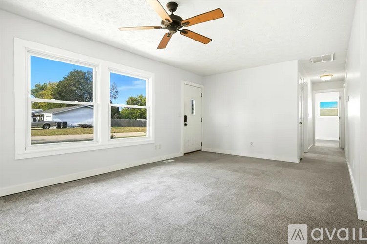 A room with a ceiling fan and two windows overlooking a house.