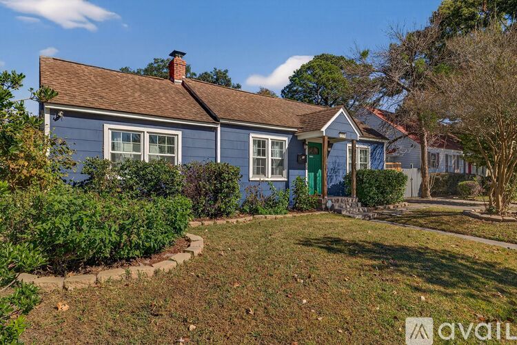 A house with a blue exterior and a green door is surrounded by a well-kept lawn.