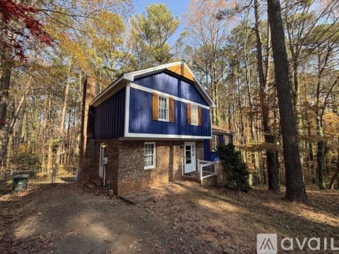 A blue house with a white door and windows is surrounded by trees.