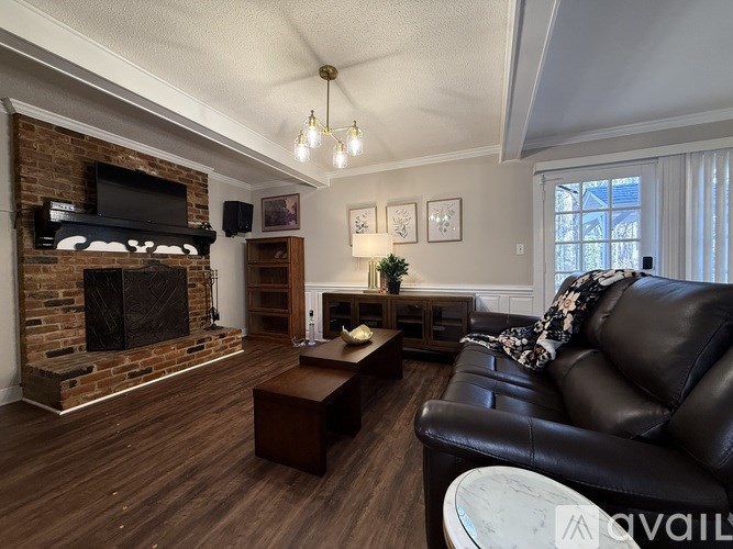 A living room with a black leather couch and a brick fireplace.