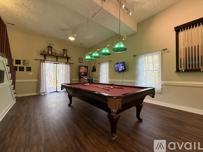 A pool table is in the middle of a room with a TV and a window.