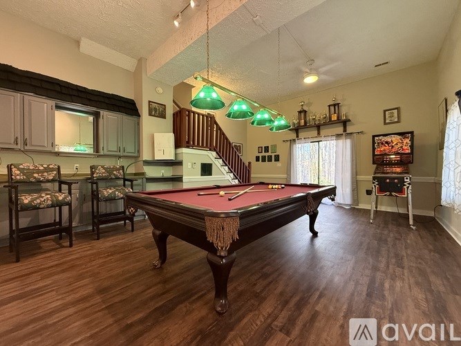 A pool table is in the middle of a room with a staircase in the background.