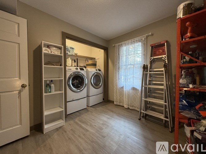 A laundry room with a washer and dryer, a ladder, and a shelf with various items.