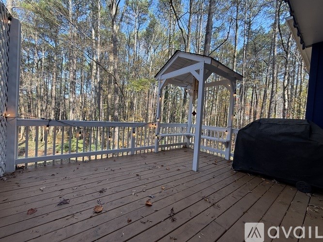 A gazebo is on a wooden deck with trees in the background.