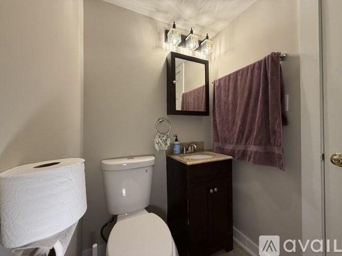 A bathroom with a toilet, sink, mirror, and towel.