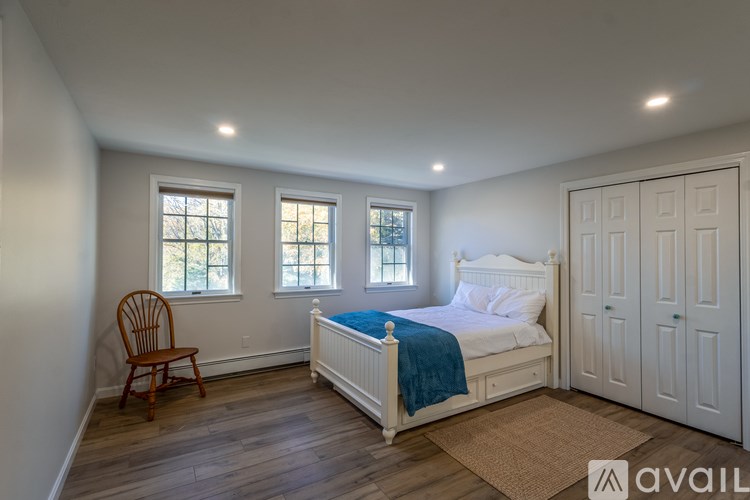 A bedroom with a bed, chair, and two windows.