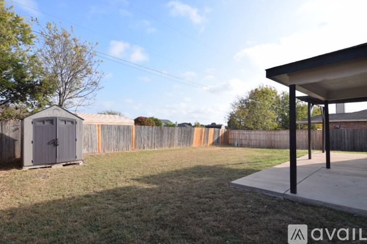 A backyard with a shed, fence, and a covered patio area.