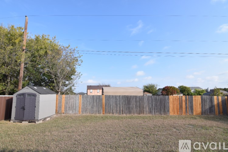 A wooden fence with a grey shed and a brown house in the background.