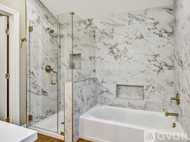 A white marble bathroom with a glass shower stall and a white bathtub.