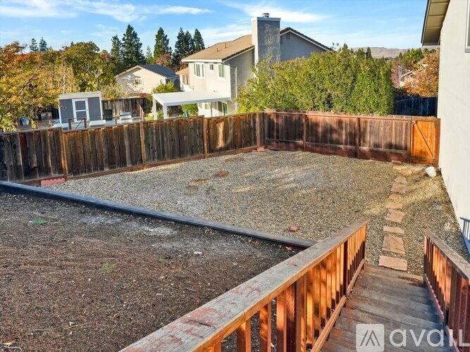 A backyard with a wooden fence and a gravel area.