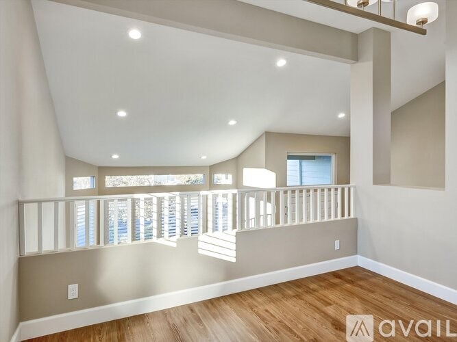 A spacious room with wooden flooring and a balcony with white railings.