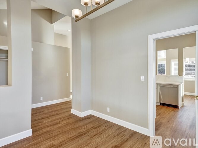 A room with wooden floors and white walls, with a doorway leading to another room.