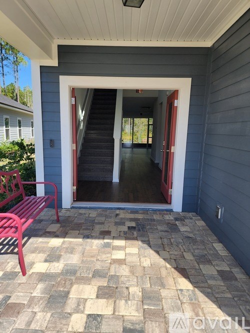 A red bench is on a patio with a doorway leading to a hallway.