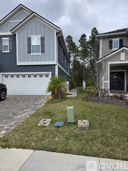 A grey house with a white garage door and a green trash can.