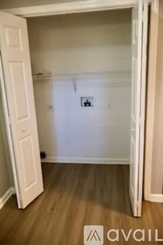 A white door is open to a room with a white wall and a wooden floor.