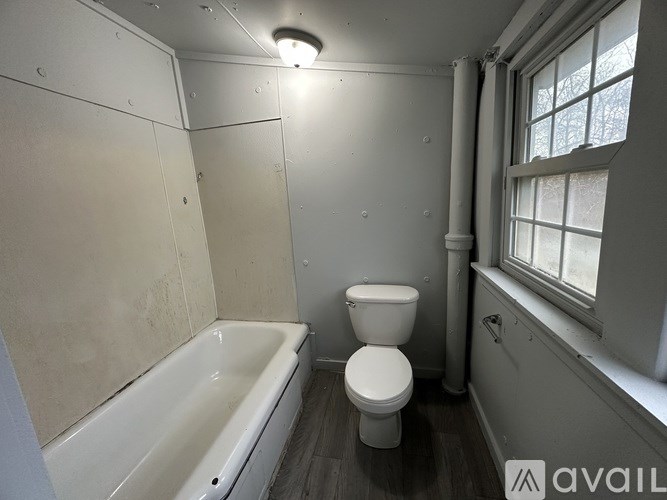 A bathroom with a toilet, bathtub, and window.