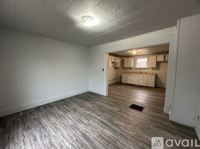 A room with wooden flooring and white walls, with a window and a door visible.