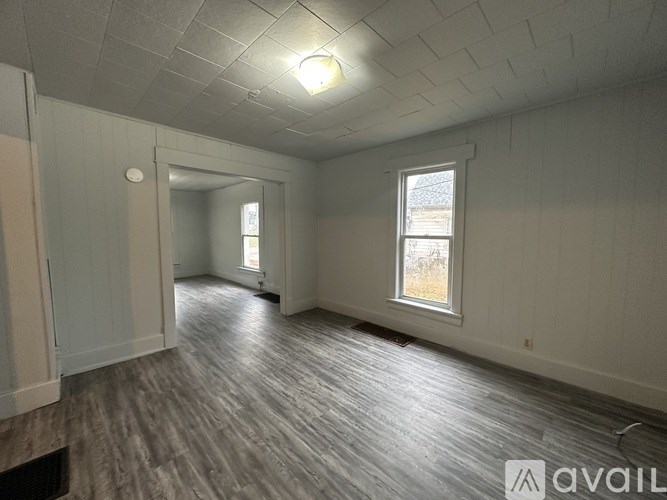 A spacious room with wooden flooring and two windows.