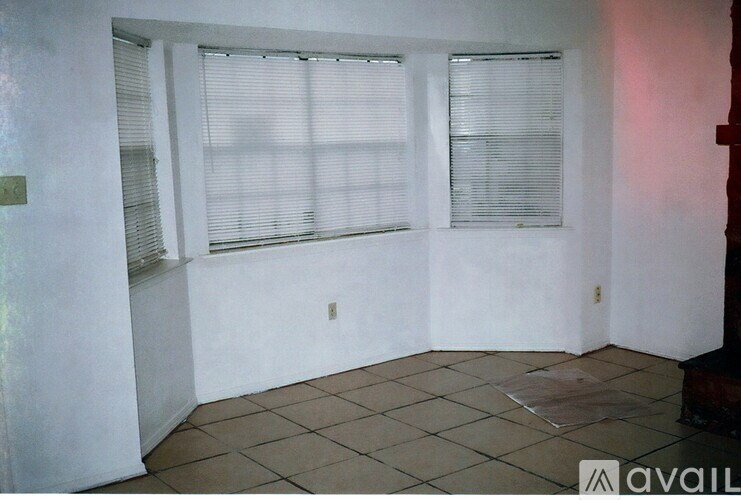 A room with a tiled floor and two windows covered with blinds.