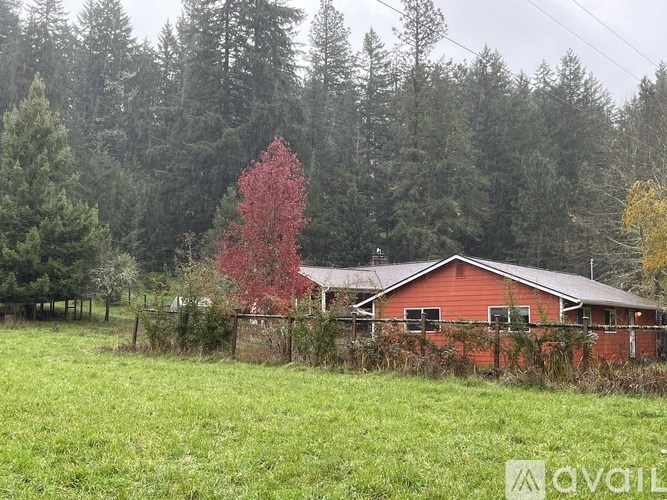 A red barn sits in a field with a forest in the background.
