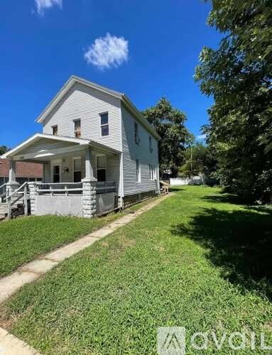 A white house with a porch and a green lawn in front.