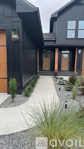 A modern house with a black exterior and a gravel pathway leading to the front door.