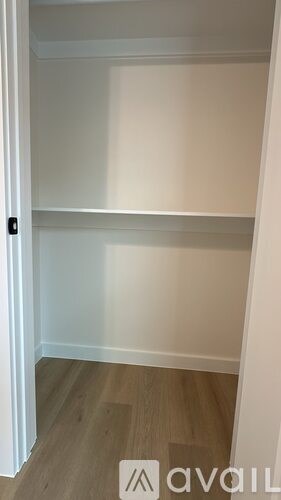 A white door with a black handle is open to a white wall and a wooden floor.