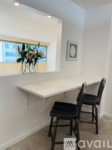 A white desk with two chairs and a vase of flowers on a windowsill.