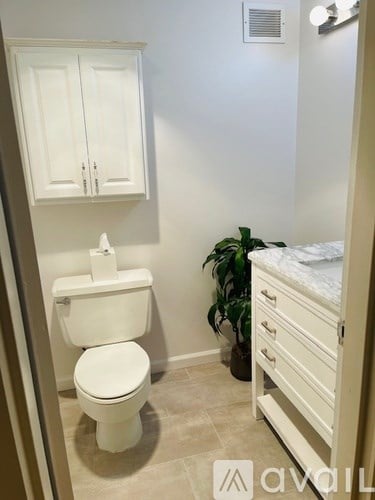 A white toilet with a white cabinet and a plant in a bathroom.