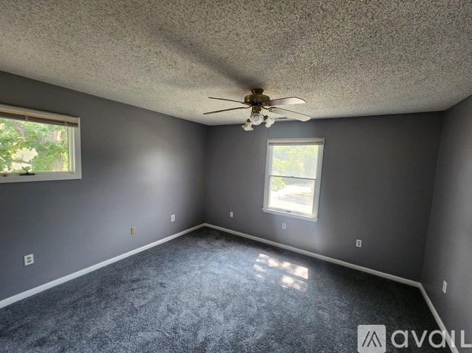 A room with a ceiling fan and two windows.