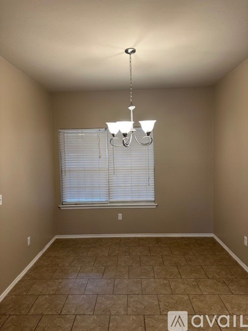 A room with a chandelier, tiled floor, and a window with blinds.