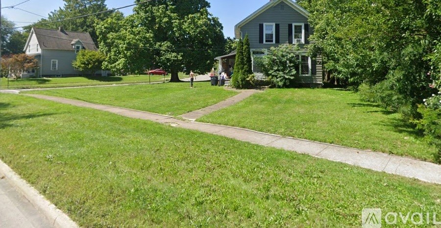 A grassy area with a house and a tree in the background.