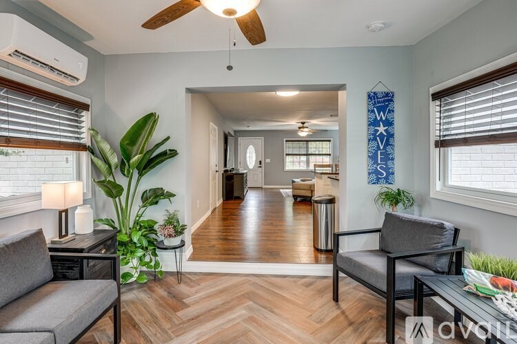 A living room with a grey couch, a black chair, a wooden floor, and a ceiling fan.