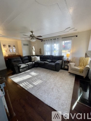 A living room with a black sectional sofa and a white rug.