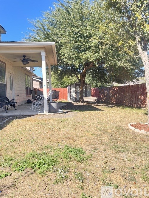 A backyard with a tree, a patio, and a fence.