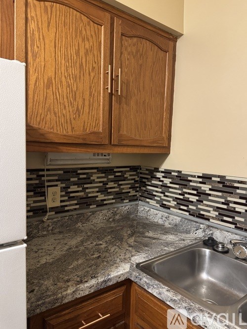 A kitchen with a white refrigerator, wooden cabinets, and a granite countertop.