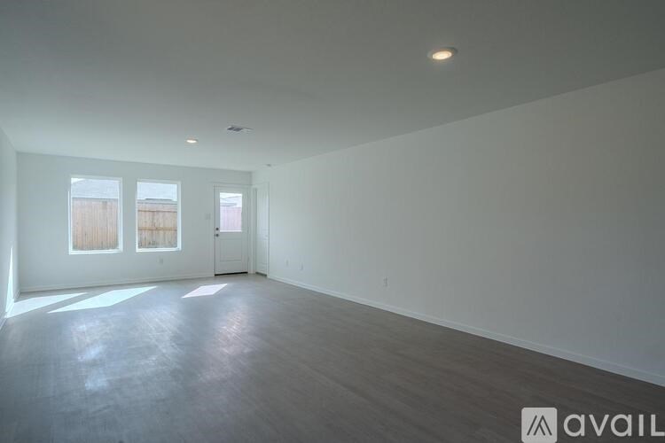 A spacious room with wooden flooring and white walls, with a window on the left side.