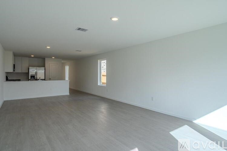 A spacious empty room with a kitchen area to the left and a window on the right.