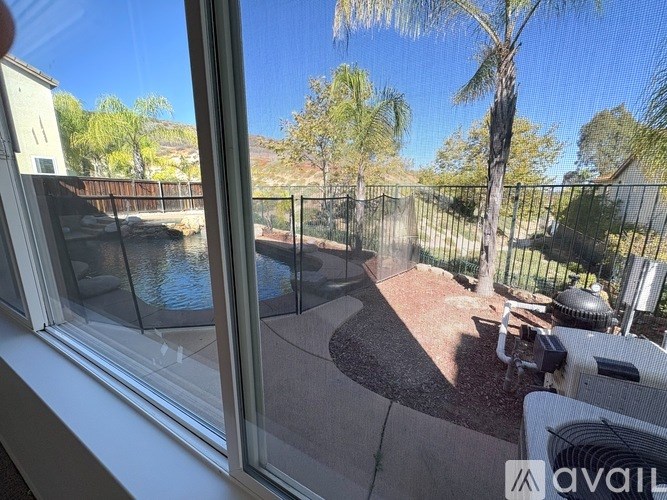 A view from a window looking out to a patio with a tree and a pool.