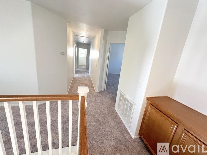 A hallway with a carpeted floor, white walls, and a wooden railing leading to a door at the end.