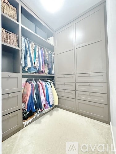 A spacious walk-in closet with clothes hanging and drawers.
