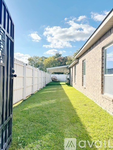 A long, narrow yard with a white fence and a brick building on the right.