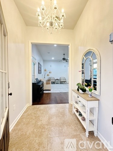 A hallway with a chandelier, a piano, and a mirror.