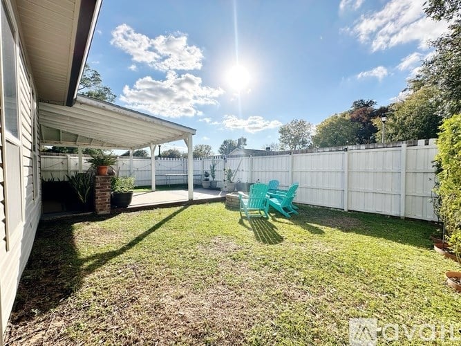 A sunny day in a backyard with a white fence, a green chair, and a potted plant.