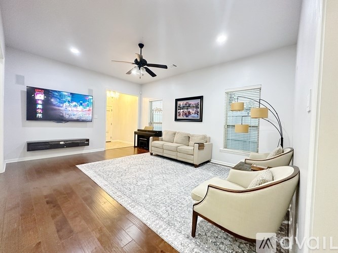A living room with a television, a couch, a chair, and a fan.