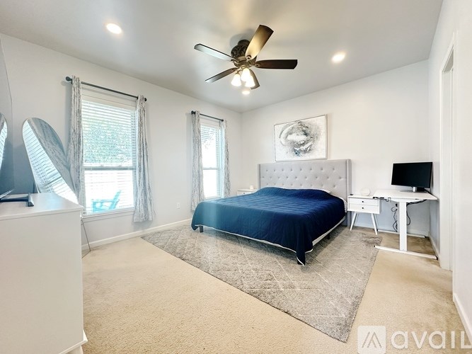 A bedroom with a bed, desk, and fan.