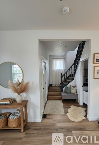 A hallway with a wooden floor, a mirror, a bench, and a rug.