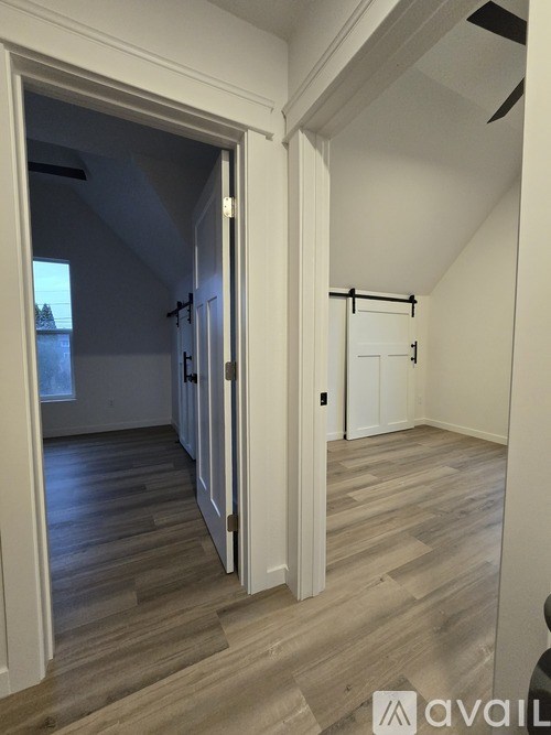 A room with a wooden floor and white walls, with a door open to another room.